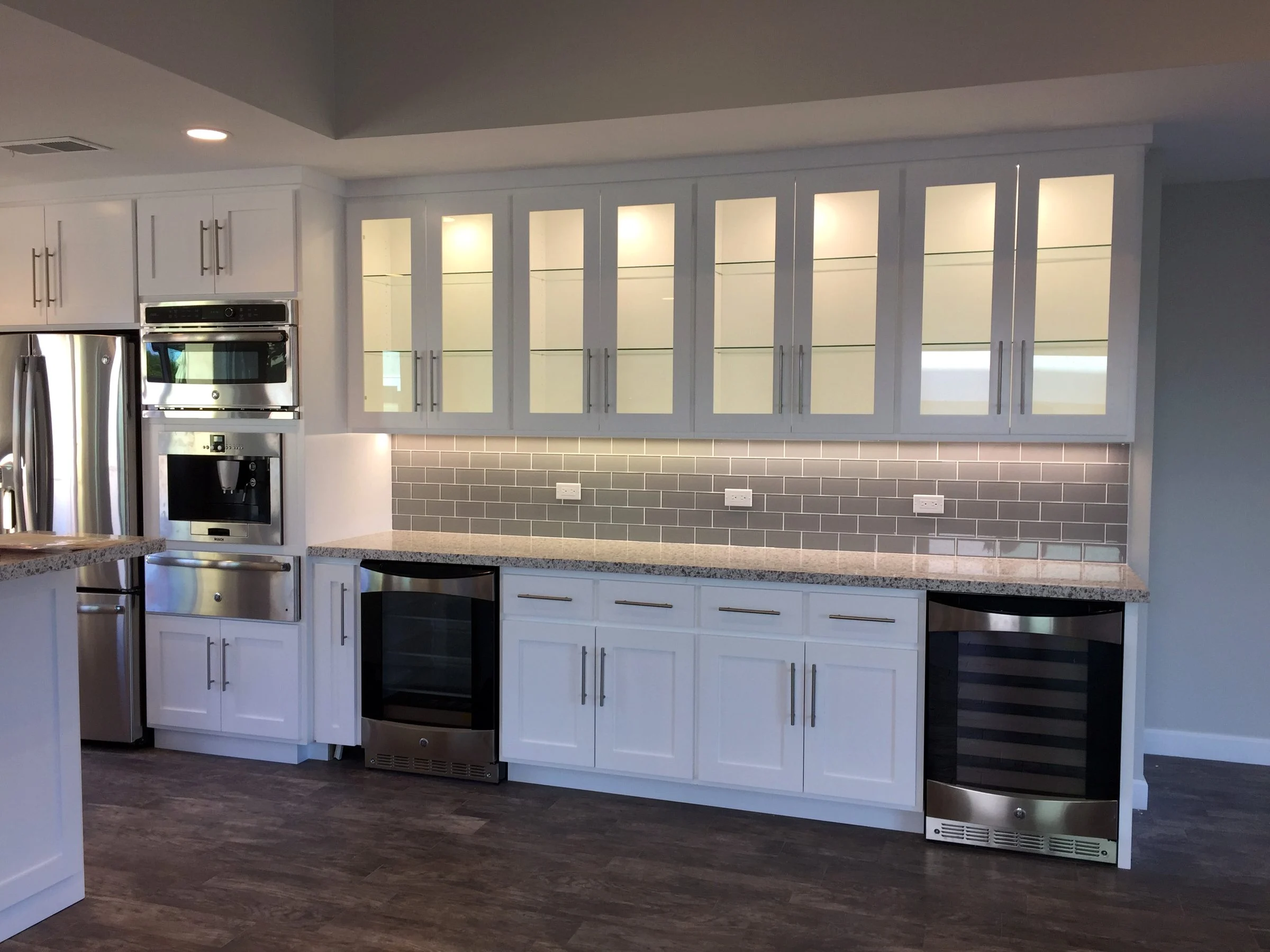 White kitchen with lit glass-front cabinets and a wine refrigerator